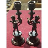 A PAIR OF BRONZE CHERUB FORM CANDLESTICKS The male figure astride waisted circular section plinth,