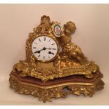 A 19TH CENTURY FRENCH ORMOLU CLOCK Figured with a putti, holding a porcelain plaque, the white