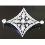 AN EDWARDIAN PERIOD PLATINUM AND DIAMOND BROOCH The pierced lozenge shaped panel with foliate
