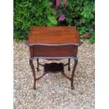 AN EDWARDIAN MAHOGANY SEWING/GAMES TABLE With a serpentine shaped lid, opening to reveal a quilted