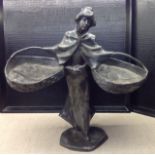 AN ART NOUVEAU SILVER PLATED FIGURE Of a woman, bearing two baskets, one over each arm, her hair