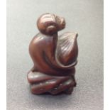 AN ANTIQUE WOODEN NETSUKE In the form of a monkey clutching a fruit in his lap, signed to underside.