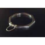 AN OCTAGONAL SILVER BANGLE The hollow hinged bangle having a box clasp and safety chain. (6.8cm)