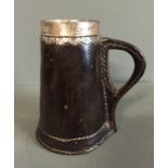 A 17TH/18TH CENTURY LEATHER TANKARD With an engraved silver rim and polished tapering body, with