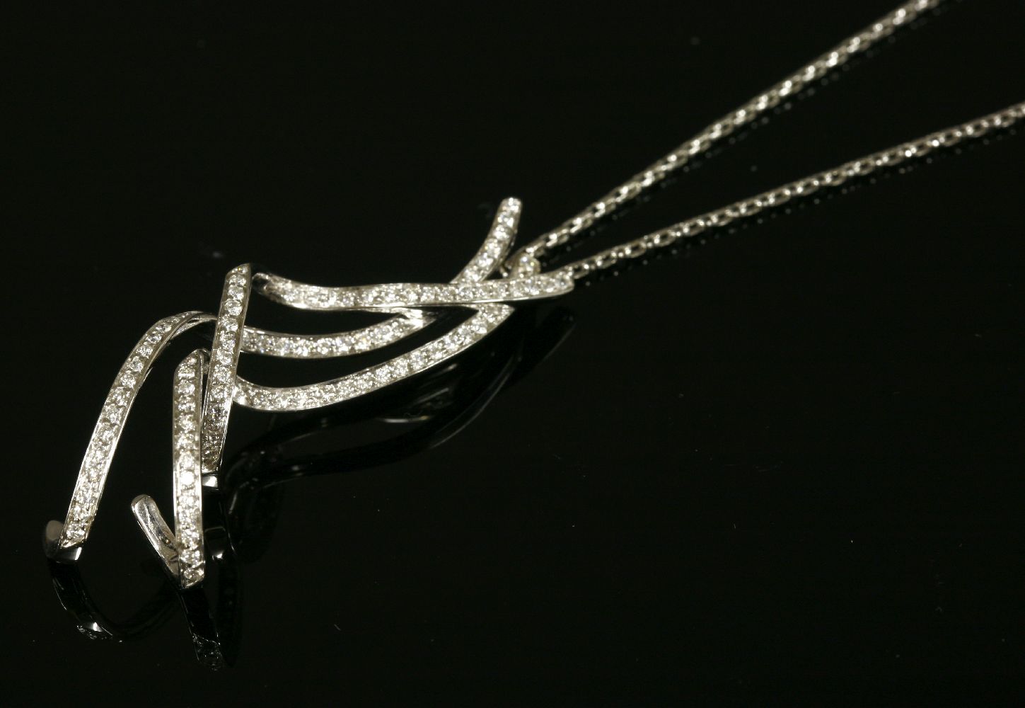 An Italian white gold diamond set pendant, with three curled ribbon strands, claw set with lines