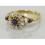 A sapphire and diamond circular cluster ring, with sapphire set shoulders, marked 18ct