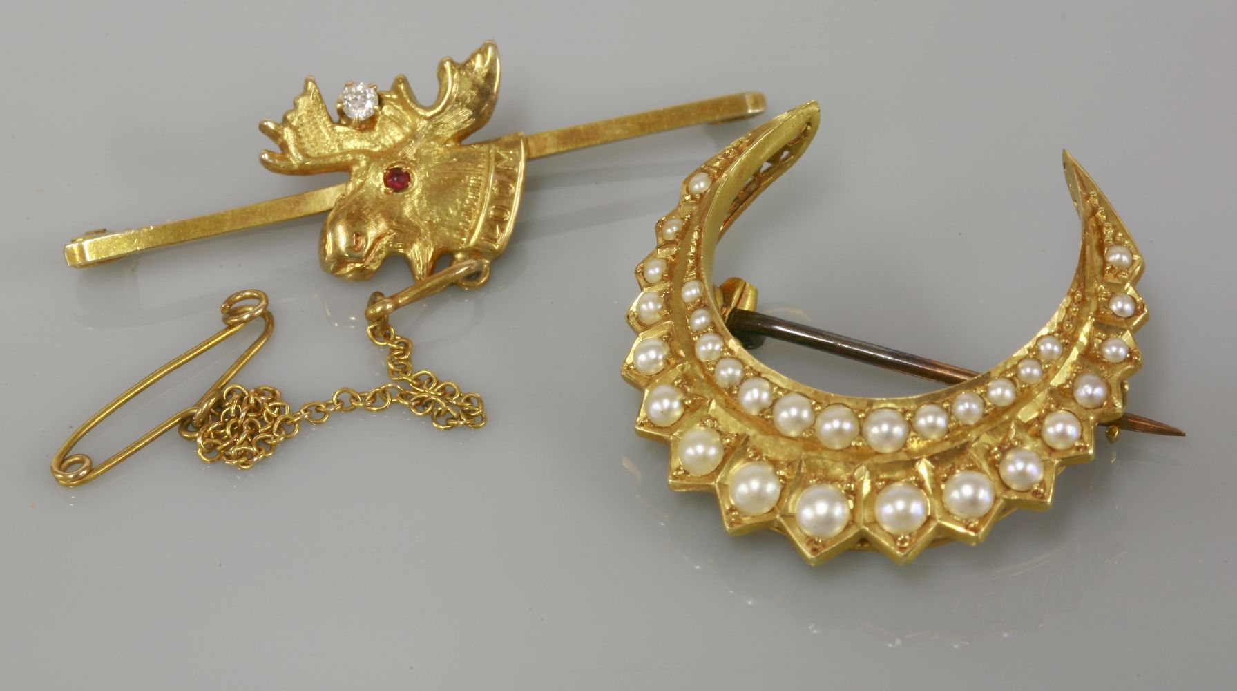 A gold split pearl crescent brooch, circa 1900, marked 18, and a 9ct gold ruby and diamond set elk