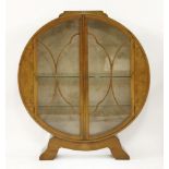 An Art Deco walnut circular display cabinet,with two glass shelves, a machine woven backboard,