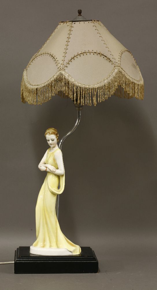 An Art Deco pottery table lamp,modelled as a lady in a yellow dress, on an ebonised plinth, with a