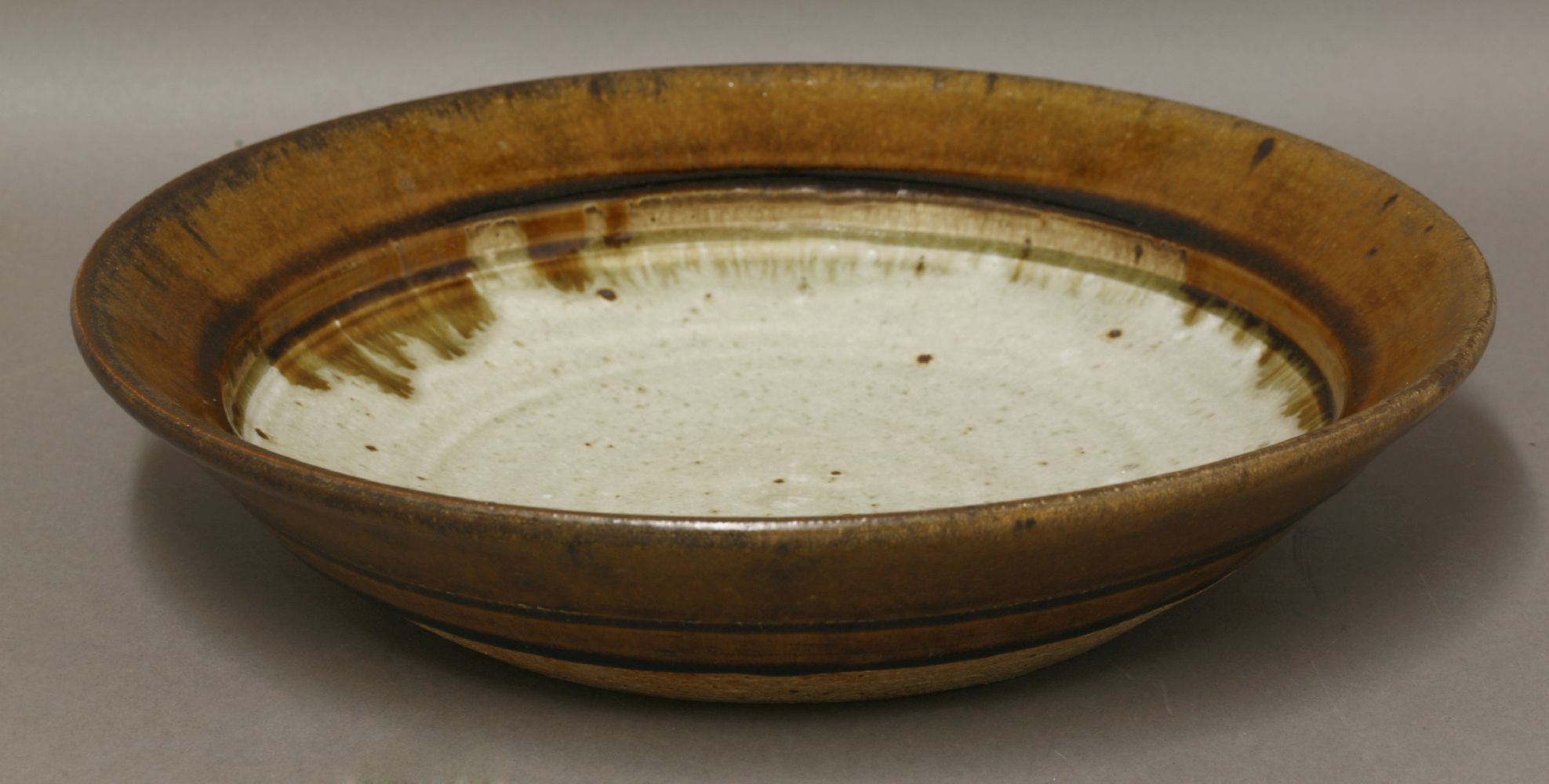 *A stoneware dish,by Richard Batterham (b.1936), with a brown-glazed rim and a light celadon centre,
