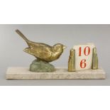 A gilt metal desk calendar,mounted with a bird beside a calendar mount, lacking cards, on a marble