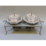 A pair of silver plated entrée dishes and covers, on a hotplate, with two burners
