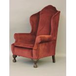 A 1920s wing armchair, on claw and ball feet, newly upholstered