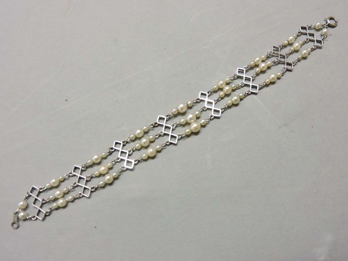 An Art Deco three row graduated cultured pearl bracelet, with pieced geometric bars stamped 9ct