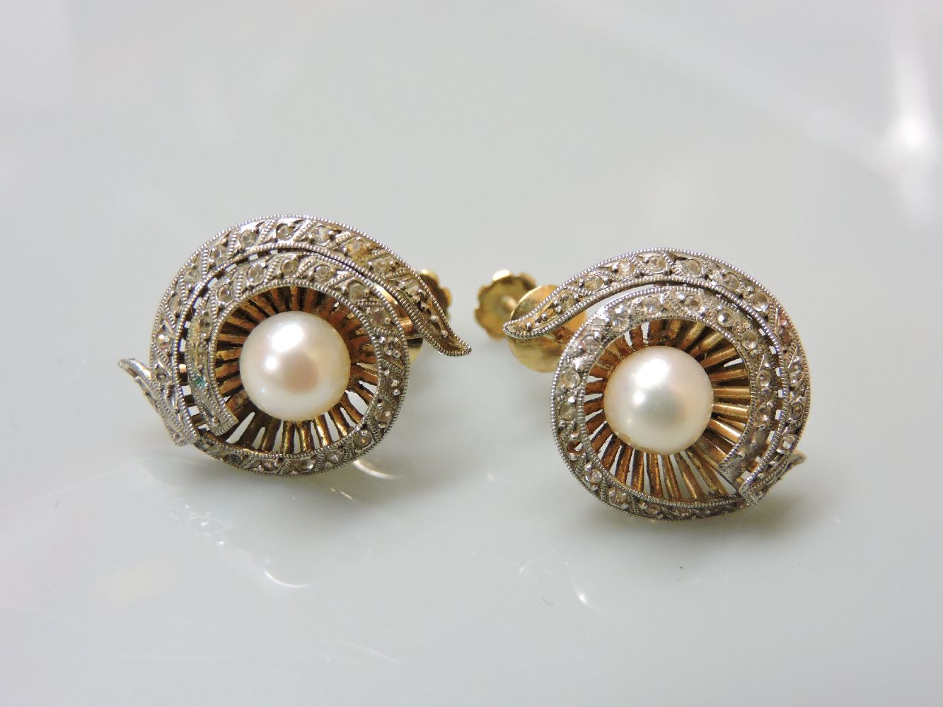 A pair of cultured pearl screw back earrings, with white stone set border, tested as approximately