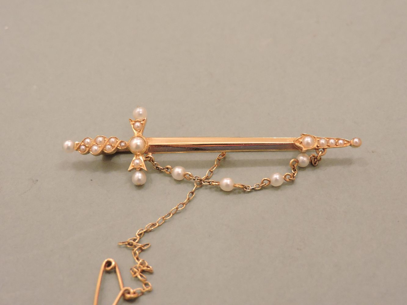 A Victorian gold sword brooch, set with split pearls, and a seed pearl chain tested as approximately