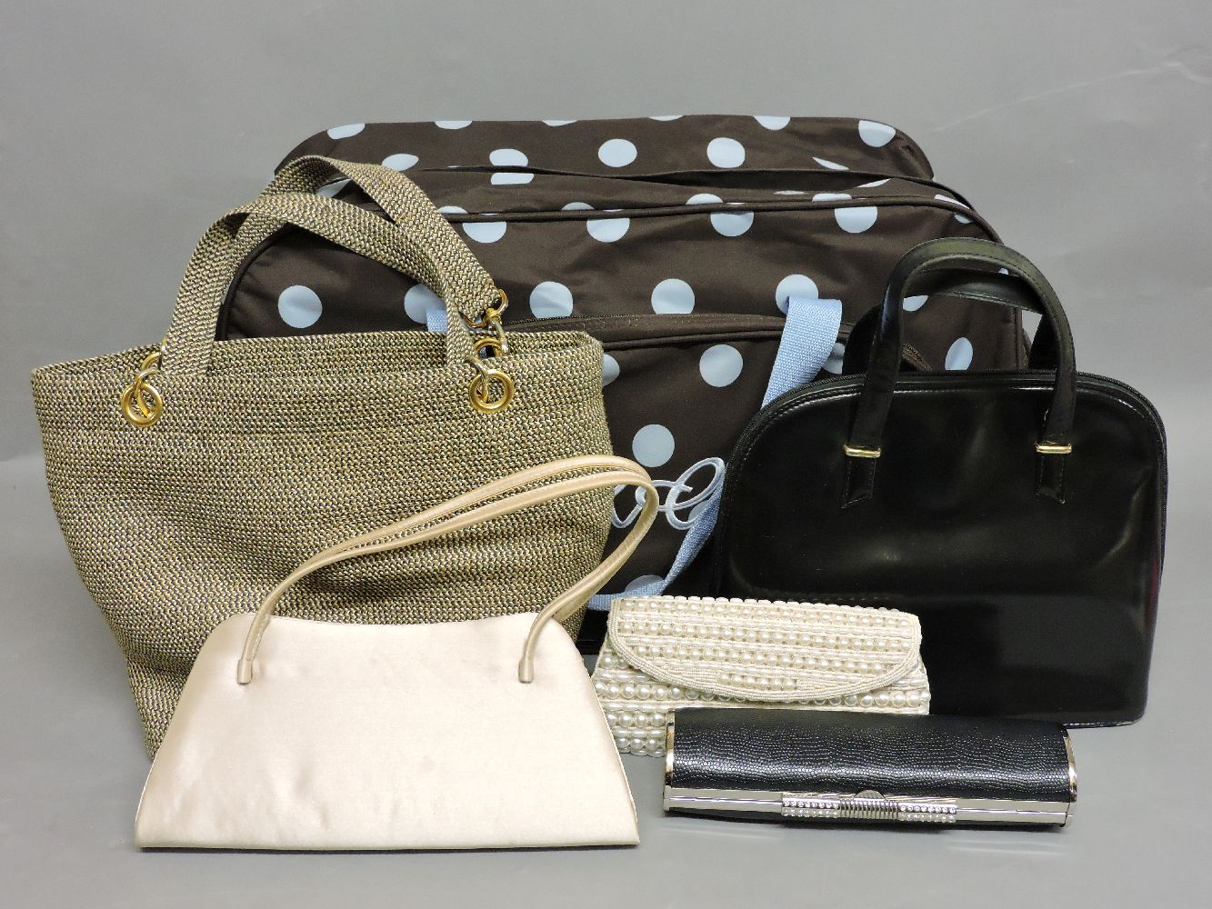 A brown and blue spotted travel bag, and four evening handbags, including a black lizard skin
