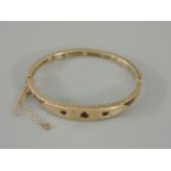 A gold hinged bangle, set with three garnets in star settings, tested as approximately 9ct gold,