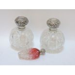 A pair of cut glass and silver mounted scent bottles, together with a cranberry glass example