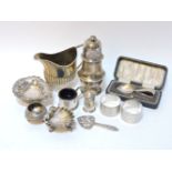 A silver caster, a silver cream jug, a shell shaped salt, napkin rings, etc