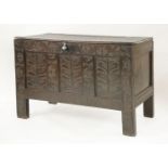 A 17th century oak coffer, the plank top over a panelled front, carved with stylised foliage,