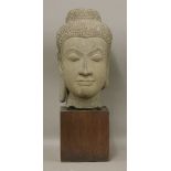 A carved stone bust of Buddha, 19th century or later, serenely modelled, on a wood block base,bust