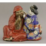 A Kutani Group, c.1880, of Daruma seated pensively in an iron-red robe, picking his teeth while a