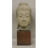 A carved stone bust of Buddha,19th century or later, serenely modelled, on a wood block base,bust