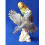 A porcelain Model of a pair of playful Budgerigars on a tree stump decorated in matt polychrome,