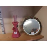 A circular toilet mirror with floral decoration together with a pink glass lamp base