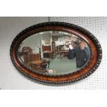 A 20th Century oval bevelled wall mirror in decorative walnut frame