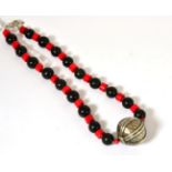 A necklace of coral beads alternating with black beads to a central white metal spherical bead