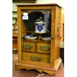 A late Victorian glazed blond oak smokers cabinet fitted with pottery tobacco jar and ashtrays