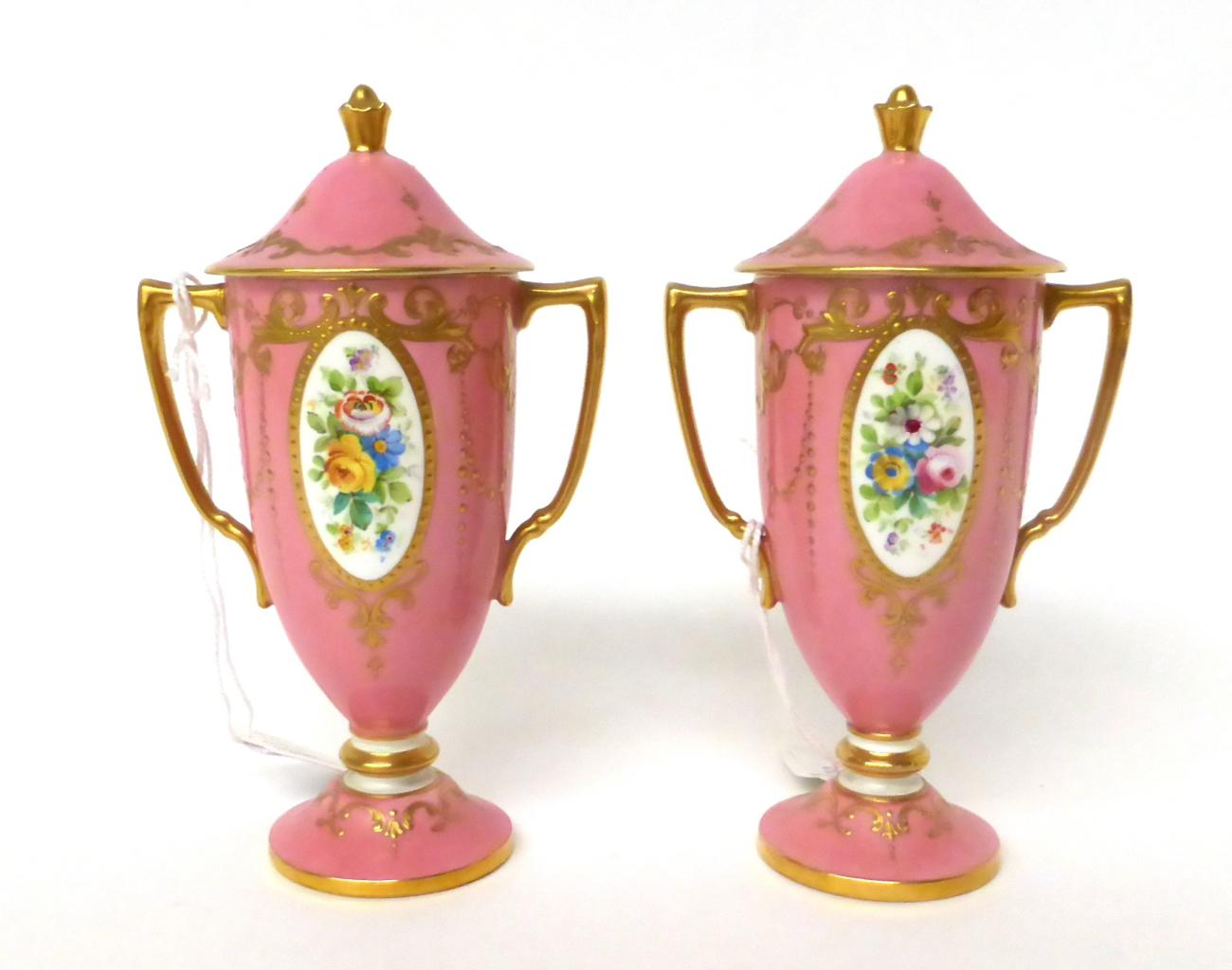 * A pair of Minton pink ground twin-handled urn shaped vases and covers decorated with flowers, 14.
