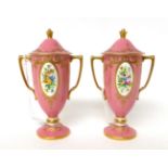 * A pair of Minton pink ground twin-handled urn shaped vases and covers decorated with flowers, 14.