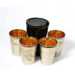 A set of four white metal and enamel stacking hunting cups, with gilt interiors, in a hide case