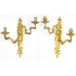 A Pair of Gilt Bronze Two-Light Wall Lights, the scroll backplates with cherubs' masks flanked by