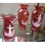 A pair of cranberry glass vases (approx 10.25" high), and another, all decorated with Mary Gregory