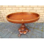 A mahogany, oval pedestal table on turned support terminating in claw feet.