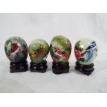 Four hand painted jade eggs with wooden stands depicting flowers and birds which represents the