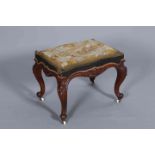 A VICTORIAN CARVED AND UPHOLSTERED STOOL, the rectangular seat with needlework landscape cover,