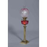 A VICTORIAN BRASS AND CRANBERRY GLASS OIL LAMP, with Corinthian column and stepped square base,