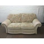 A beige floral settee with cream leather trim