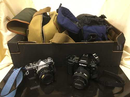 A box of camera bags, Olympus OM-1 camera with lens, Nikon F90X camera, Sony cam corder,