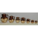 Graduated set of six Doulton Lambeth stoneware jugs of baluster form with brown glazed necks,