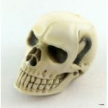 A carved ivory memento mori paperweight in the shape of a skull with a snake