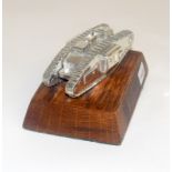A white metal WW1 tank mounted on a wood base. 5.5cms high by 10.5cms long overall
