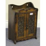 An early 20th Century oak hanging smoker's cabinet, the swan neck pediment above a pair of carved