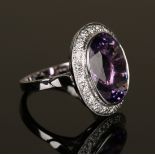 An 18ct white gold, amethyst and diamond oval cluster ring, collet set with the oval cut amethyst in