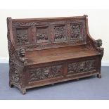 A late 19th Century oak box seat settle, the panelled back carved with four interior tavern
